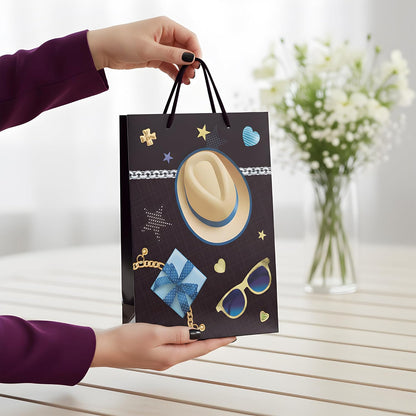 Person holding a decorative gift bag with a hat, sunglasses, and other items on a blurred background