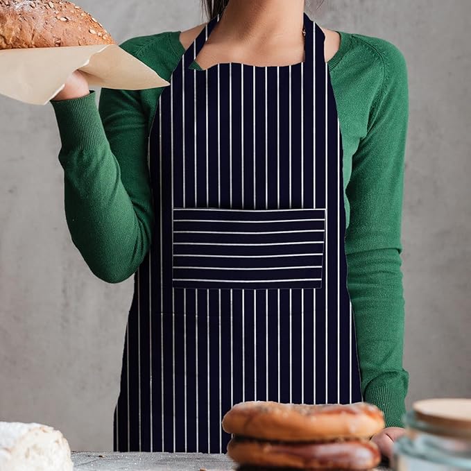 Person wearing a black apron with white stripes, holding bread, standing behind a counter with pastries.
