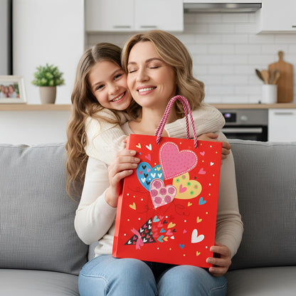 Woman and young girl holding a red gift bag with heart designs in a kitchen.
