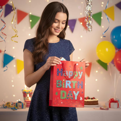 Young woman holding a 'Happy Birthday' gift bag in a festive setting with balloons and decorations.